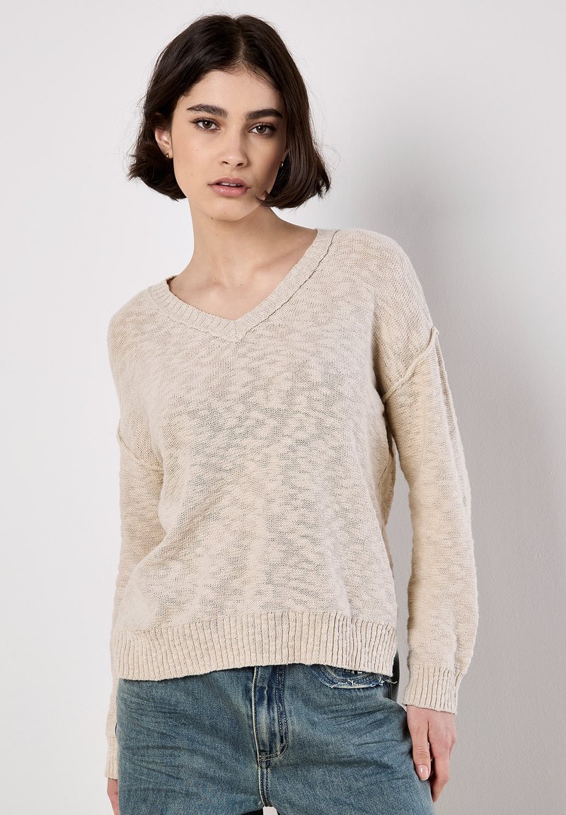 Lichtbeige V-hals trui met een losse pasvorm, geribde manchetten en zoom. Gebreid textuur met subtiele kleurvariaties. Gecombineerd met denim jeans.