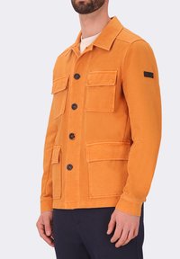 Giacca di cotone arancione con collo, chiusura a bottoni, quattro tasche frontali e un'etichetta nera sul manica. Tessuto morbido, design aderente.