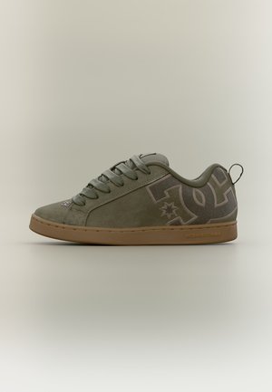 Vue latérale d'une basket vert olive avec semelle marron, lacets et un logo stylisé sur le talon et le panneau latéral.