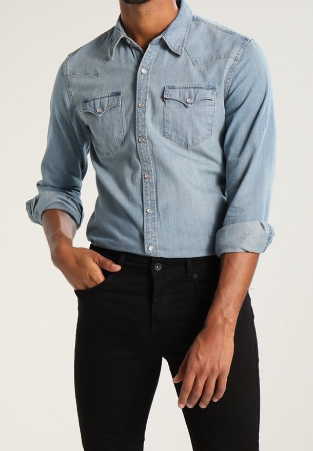 Ljusblå denimskjorta med uppvikt lång ärm, två bröstfickor och knappstängning; matchad med åtsittande svarta jeans.