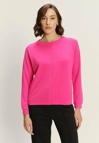 Felpa fucsia con maniche lunghe e scollatura a girocollo, caratterizzata da una superficie liscia e una vestibilità comoda, abbinata a pantaloni neri.