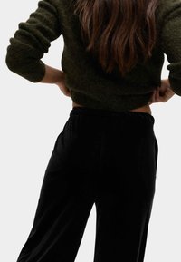 Ciemnozielony sweter dzianinowy o fakturze, z długimi rękawami, zestawiony z czarnymi, wysokim stanem, aksamitnymi spodniami z elastycznym paskiem.