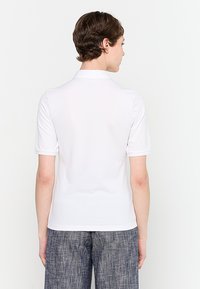 White short-sleeve polo shirt with a collar, designed in a smooth fabric. Back view shows a fitted shape with no visible accents.