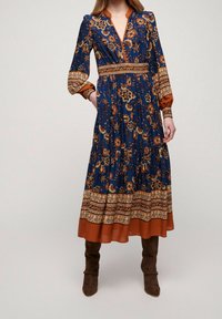 Lång blå blommig klänning med orange detaljer, med V-ringning, långa ärmar och en flerlagerskjol. Strukturerad tyg med mönstrade detaljer.