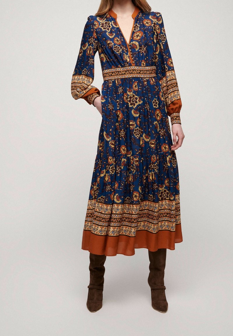 Lång blå blommig klänning med orange detaljer, med V-ringning, långa ärmar och en flerlagerskjol. Strukturerad tyg med mönstrade detaljer.