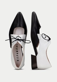Chaussures en cuir noir et blanc avec un bout pointu, un design découpé et des lacets noirs, dotées d'un petit talon carré et d'une texture lisse.