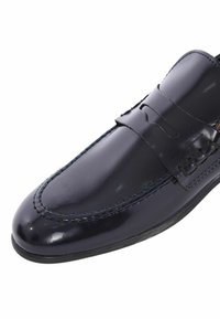 Mocassino in pelle verniciata blu navy con finitura liscia, cuciture decorative e dettaglio a fascia sul dorso del piede. Design a punta arrotondata.