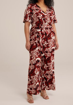 Mujer con un mono de pierna ancha con estampados florales en rojo, blanco y negro, y sandalias de cuña beige con tiras.