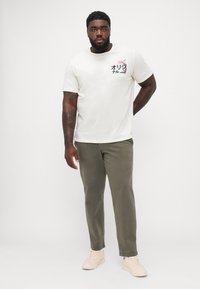 Korte mouwen off-white t-shirt met kleurrijke graphic op de borst, gecombineerd met olijfgroene broek en beige sneakers. Soepele stoftextuur.