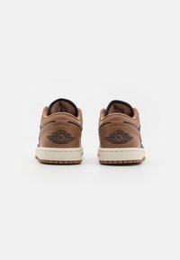 Brązowe skórzane sneakersy o niskim kroju, z czarnymi akcentami i wytłoczonym logo na pięcie. Kremowa podeszwa z teksturowanym bieżnikiem.