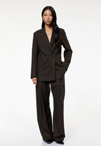 Braunes Nadelstreifenanzug mit einem doppelt knöpfbaren Blazer und weit geschnittenen Hosen. Glatte Textur mit feinen, kontrastierenden Streifen.