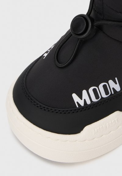 Černé Moon Boot s bílou podrážkou, které mají elastické šněrování s tahem a text "MOON" na horní části blízko špičky.