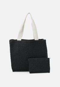 Černá tkaná taška na rameno s krémovými látkovými ušima a odpovídající černou tkanou zipovou kapsou vpředu, na bílém pozadí.