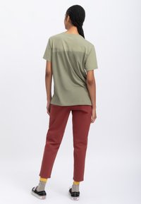 T-shirt in cotone verde oliva con vestibilità rilassata, maniche corte e colletto arrotondato; abbinato a pantaloni color ruggine e sneakers nere.