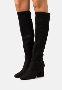 Botas negras por encima de la rodilla de suave ante, con punta afilada y tacón grueso. Textura suave con acentos mínimos.