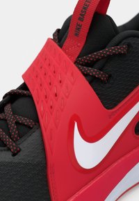 Melna Nike basketbullu apavi ar teksturētu virsotni, sarkaniem akcentiem, dimanta raksta zoli un balto Swoosh logotipu.
