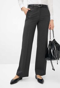 Wijde, donkergrijze broeken met een gladde textuur, voorzien van voorkruimelzakken en een zwarte riem. Gekleed met zwarte ballerina's en een zwarte tas.