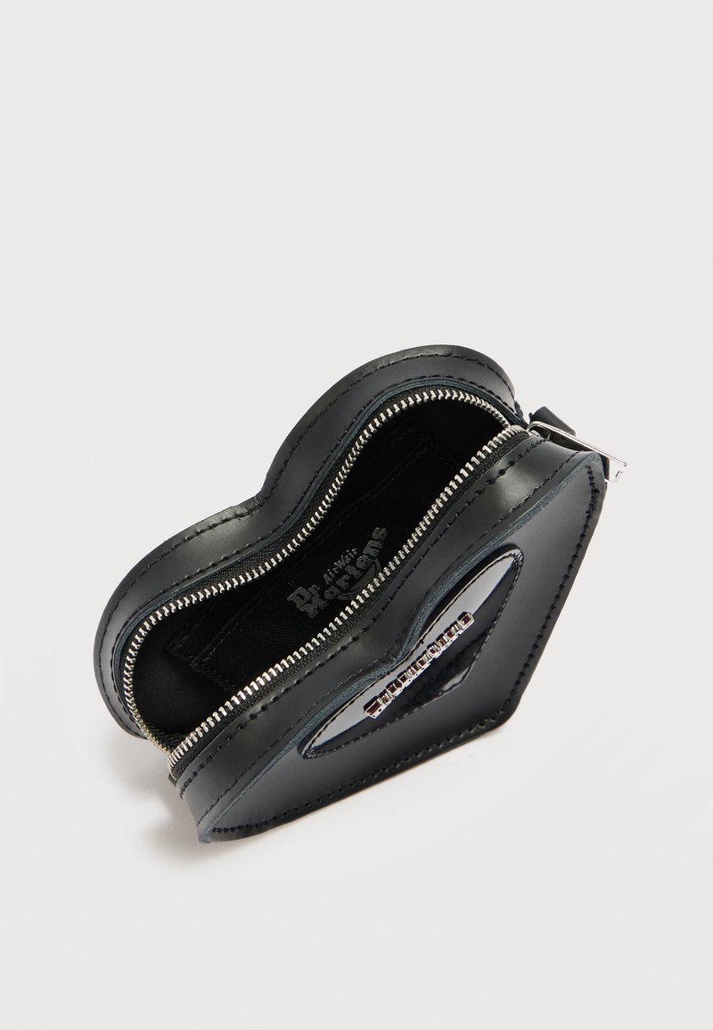Black leather heart-shaped coin purse with silver zipper partially open, showing brand logo patch inside and metal plaque on front.