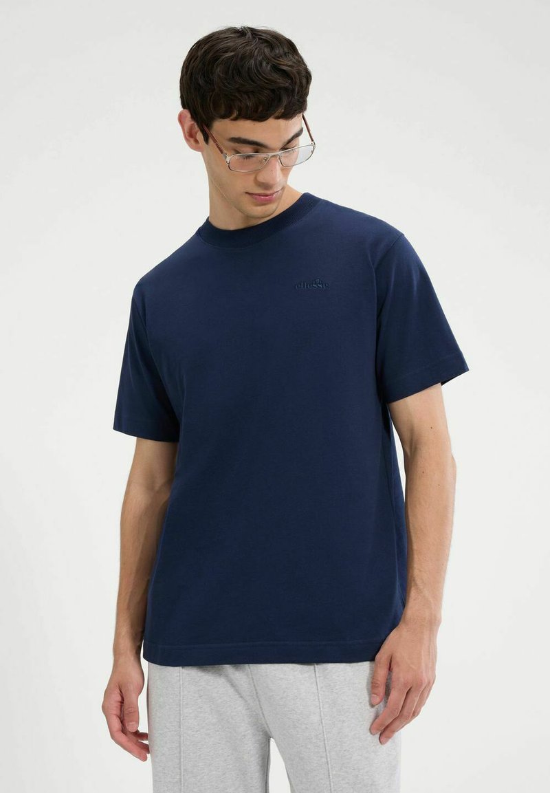 Camiseta de algodón azul marino con cuello redondo y mangas cortas. Presenta un sutil bordado de logo en el pecho. Ajuste suave y relajado.