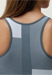 Šedý sportovní tílko s texturovanými panely v různých odstínech šedé a bílé, s výstřihem do véčka a štíhlými ramínky.
