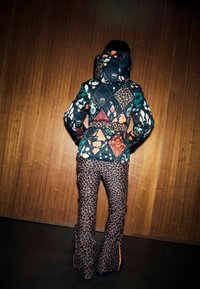 Kolorowa, wzorzysta zimowa kurtka z geometrycznym wzorem i motywami natury, połączona z spodniami w panterkę oraz zamkami błyskawicznymi przy mankietach.