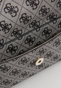 Bolsa de tela gris con un diseño estampado en negro, con cierre metálico a presión y textura suave. Incluye una correa de hombro removible.