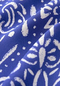 Blauer Stoff mit weißen abstrakten Mustern, die geschwungene Linien und Punkte beinhalten, mit einer glatten Textur und einem leichten Glanz.