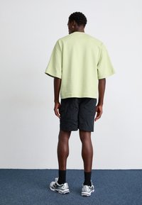 T-shirt vert clair oversize à manches courtes, associée à un short noir. La tenue est complétée par des chaussures de sport grises et des chaussettes noires.
