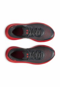 Grijze sport schoenen met een ademend mesh bovenwerk en een rode zool. Heeft tonale veters en een prominent logo op de zijkant. Lichtgewicht ontwerp.
