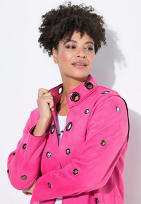 Svetle růžová bunda z jemného materiálu, se sečenými černými kroužky kolem límce a rukávů, se strukturálním designem.