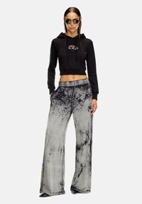 Zwarte cropped hoodie met uitgesneden detail aan de voorkant, gecombineerd met grijze wijde broek met een versleten textuur en zijzakken.