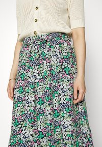 Saia maxi floral preta, com padrões em verde, branco e rosa. Cintura elástica com cordão, design em camadas, tecido leve.