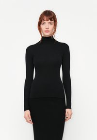 Mustra mustriga turtleneck-sveter mustas, millel on pikad varrukad, sobiv siluett ja pehme tekstuur, koos vastava musta sobiva seelikuga.
