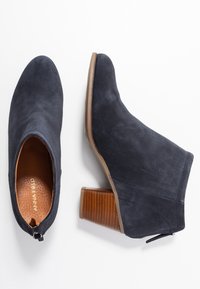 Stivaletti alla caviglia in pelle scamosciata blu scuro con punta arrotondata, forma curva e tacco a blocco marrone testurizzato. Presentano una chiusura con zip sul retro.