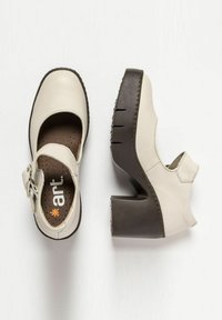 White leather Mary Jane shoes with a brown chunky heel, buckle detail, and perforated insole. Unique cutout design on the side.