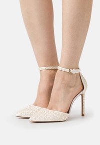 Scarpe bianche con tacco alto e punta affusolata, con un motivo testurizzato di piccole perle e una delicata cinghia alla caviglia con una fibbia metallica.