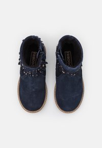 Bottines en suede bleu avec des franges décoratives, une fermeture éclair latérale et une semelle en caoutchouc brun clair. Intérieur doublé pour le confort.