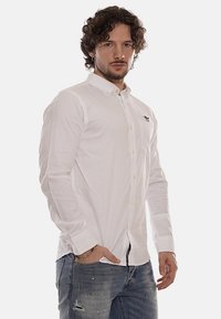 Camicia bianca a maniche lunghe con bottoni, realizzata in un leggero tessuto morbido, caratterizzata da un piccolo logo ricamato sul petto e polsini con bottoni.