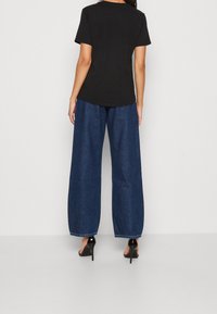 Camiseta negra de manga corta combinada con pantalones de mezclilla oscuros de pierna ancha y tacones negros. Costuras visibles en los pantalones, tejido suave de la camiseta.