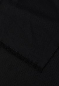 Černý šátek s texturovaným vzorem a jemně třepeným okrajem. Materiál působí měkce a lehce.