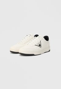 Weiße Sneaker mit niedrigem Schaft, schwarzer Innenausstattung, schwarzen Sohleinfassungen und "GUESS"-Logo auf dem seitlichen Dreieck-Patch, auf weißem Hintergrund präsentiert.