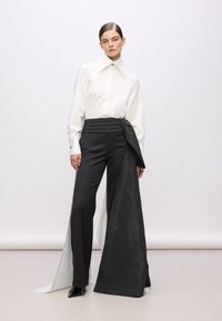 Weißes Hemd mit schimmerndem Finish, kombiniert mit schwarzen hochtaillierten Hosen mit einem drapierten Seitenelement und plissiertem Bund.