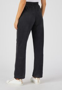 Zwarte fleece sweatpants met een ontspannen pasvorm, een elastische tailleband en zijzakken, gecombineerd met witte sneakers met gouden accenten.