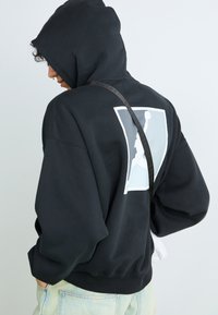 Black hoodie made of cotton blend with a large white logo on the back. Designed with a kangaroo pocket and adjustable drawstring hood.