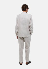 Chemise rayée de couleur claire et pantalon assorti en tissu texturé, avec des manches longues et des boutons aux poignets, associés à des sandales.