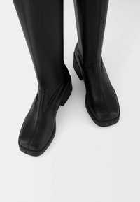 Black leather knee-high boots with a square toe, featuring a smooth texture, minimal stitching, and a low block heel.