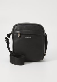 Borsa a tracolla in pelle nera con superficie testurizzata, chiusura con zip e tracolla regolabile. Presenta una tasca frontale e una marcatura in argento.