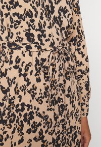 Béžové šaty s černým a hnědým leopardím vzorem, s páskem na zavazování v pase a knoflíkovými detaily, vyrobené z texturované látky.