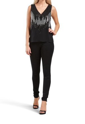 Top senza maniche nero con scollatura a V, decorato con un motivo di perline, abbinato a jeans skinny neri e sandali con tacco neri.
