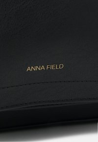 Černá umělá kůže s texturovaným povrchem, zdobená zlatým nápisem "ANNA FIELD". Čisté linie a jemné detaily švů design zdokonalují.